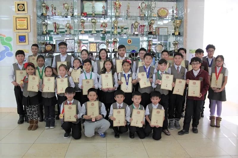 低年级学生手持证书，站在学校奖杯陈列柜前