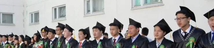 Малгай, нөмрөг өмссөн төгсөгчид сургуулийн гадаа эгнэн зогсож байна